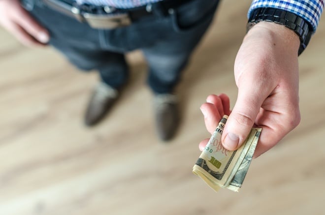 Man holding $10 bill in outstretched hand